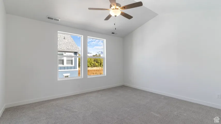 Unfurnished room with light colored carpet, vaulted ceiling, and ceiling fan