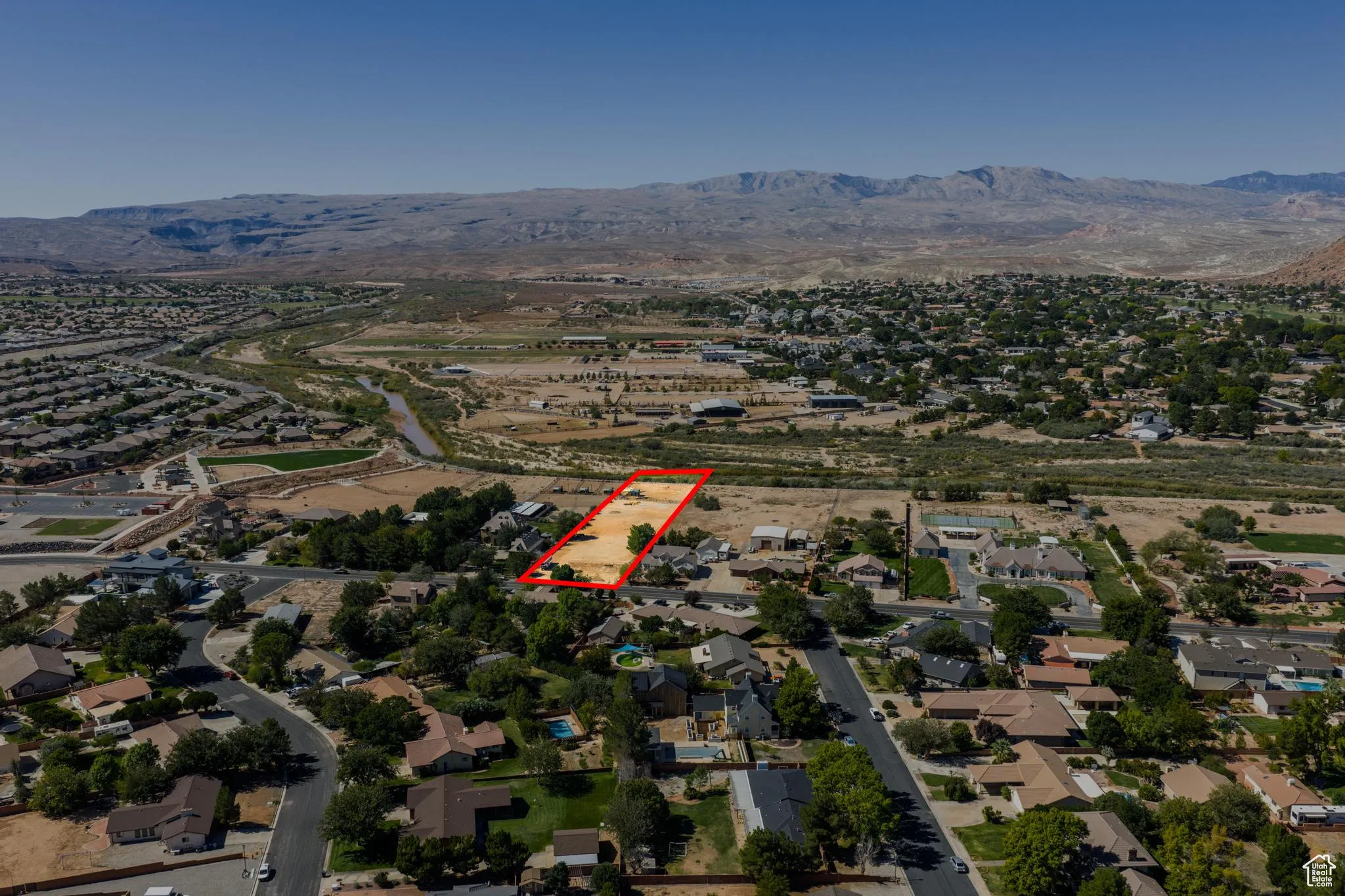 Aerial view of property and surrounding area with nearby suburban area, property parcel outlined, and a mountain backdrop