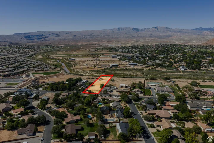 Aerial view of property and surrounding area with nearby suburban area, property parcel outlined, and a mountain backdrop