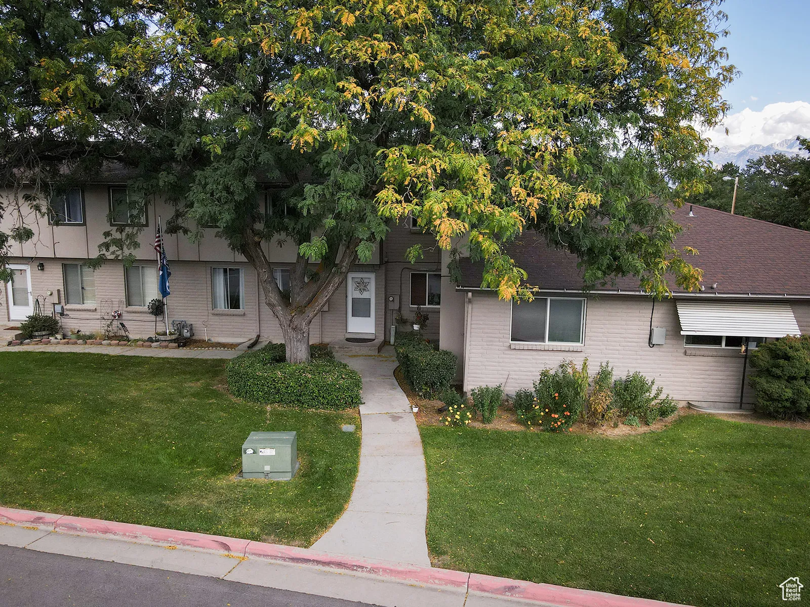 View of front of home with large shade tree and views to the golf course.