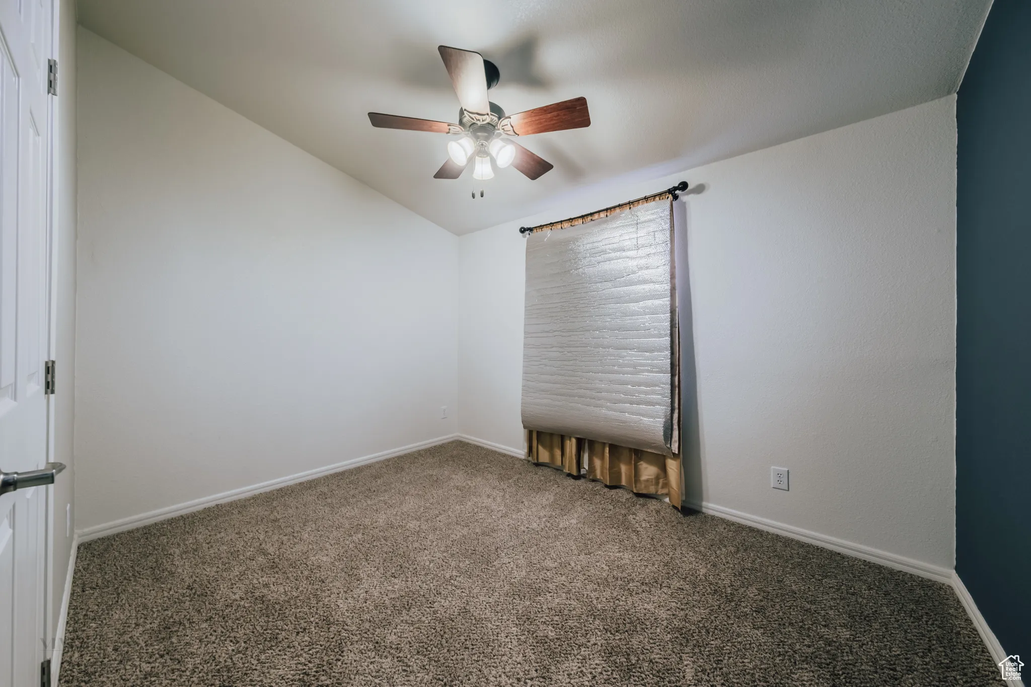 Carpeted empty room featuring lofted ceiling and a ceiling fan