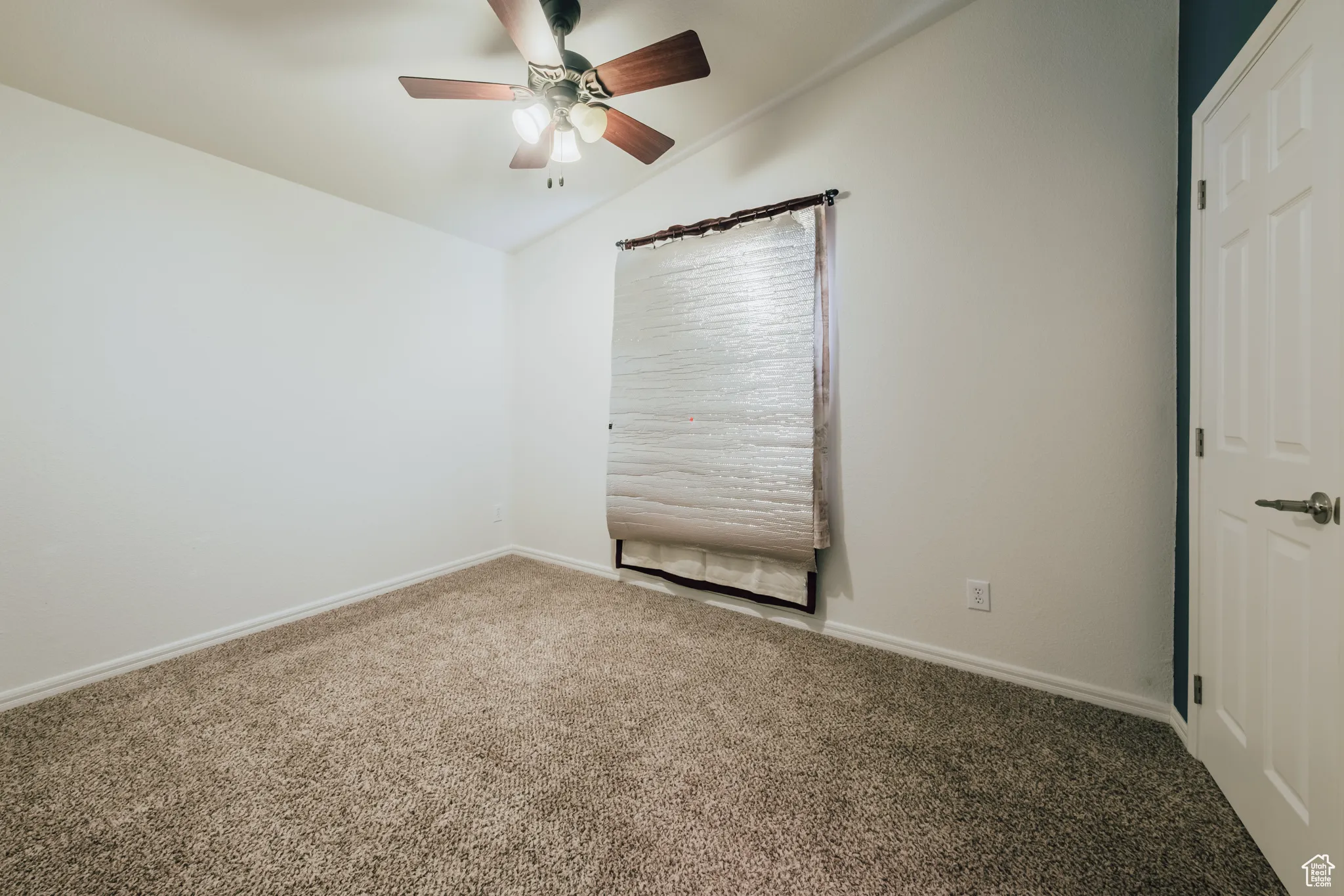 Empty room with vaulted ceiling, carpet floors, and ceiling fan