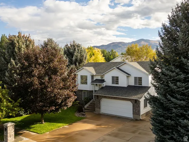 View of front of home featuring a mountain view, driveway, roof with shingles, an attached garage, and a front lawn