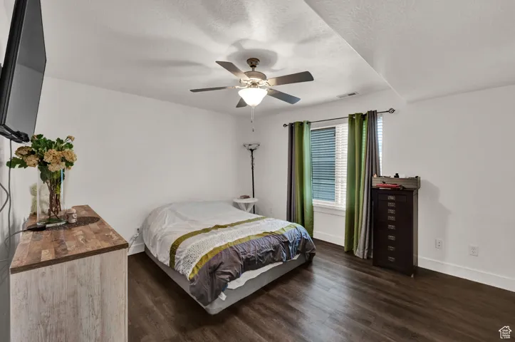 Bedroom with dark wood-type flooring, a textured ceiling, and a ceiling fan