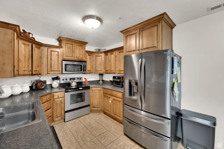 Kitchen with dark countertops, stainless steel appliances, a textured ceiling, light tile patterned floors, and brown cabinets