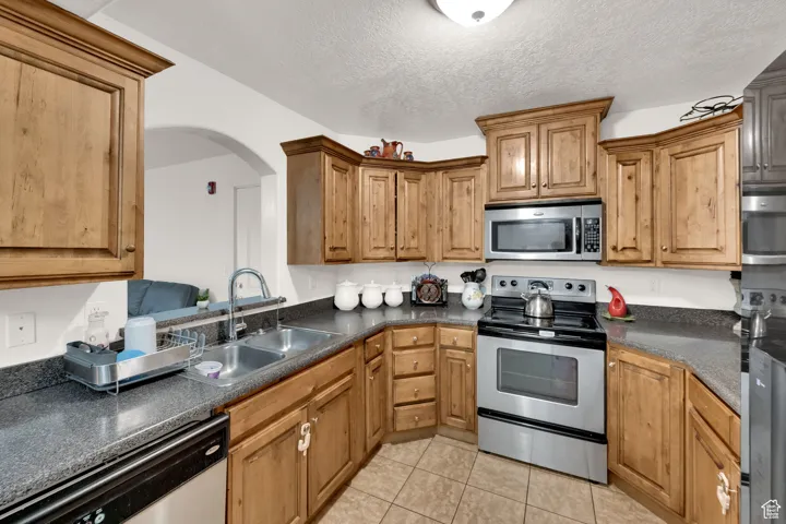 Kitchen featuring stainless steel appliances, a textured ceiling, light tile patterned floors, and brown cabinetry