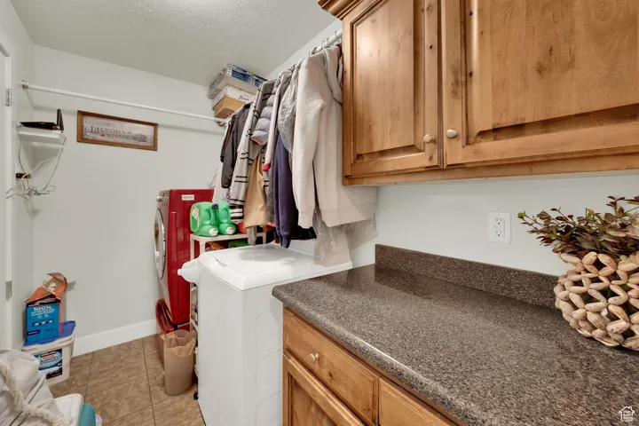 Washroom with a textured ceiling, light tile patterned flooring, cabinet space, and washing machine and dryer