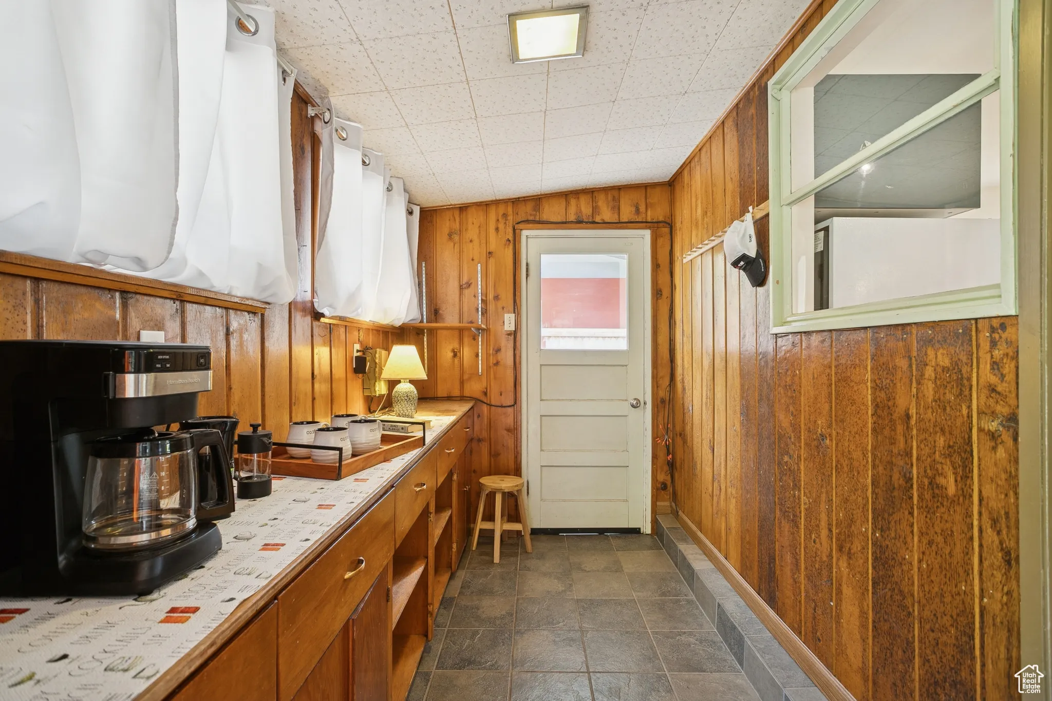 Kitchen featuring light countertops, wooden walls, brown cabinetry, and dark stone finish floors