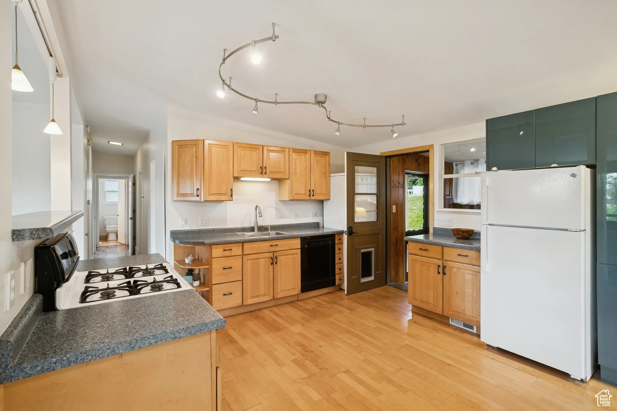 Kitchen with white appliances, dark countertops, vaulted ceiling, light wood-type flooring, and decorative light fixtures