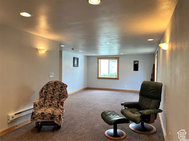 Living area with carpet flooring, a baseboard heating unit, a textured ceiling, and recessed lighting