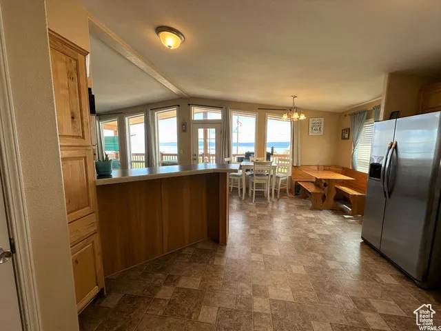 Kitchen featuring stainless steel fridge with ice dispenser, stone finish floors, a peninsula, a chandelier, and hanging light fixtures