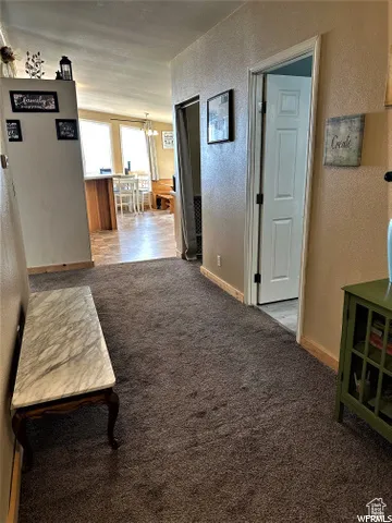Hall featuring a textured wall, dark colored carpet, and a chandelier