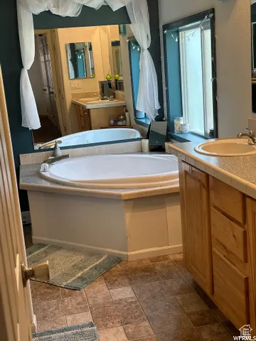 Bathroom featuring two vanities, a bath, and dark stone finish flooring