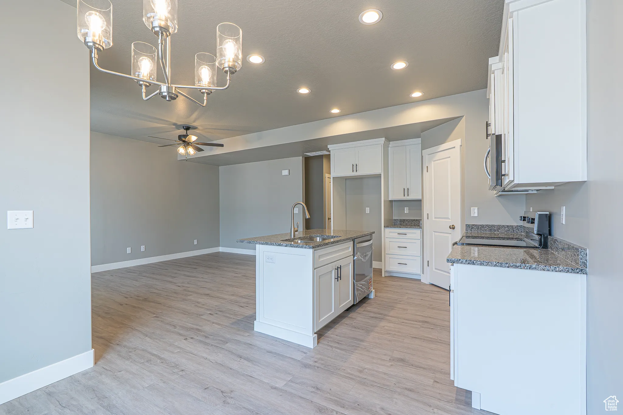 Kitchen featuring a ceiling fan, hanging light fixtures, a center island with sink, recessed lighting, and dark stone counters