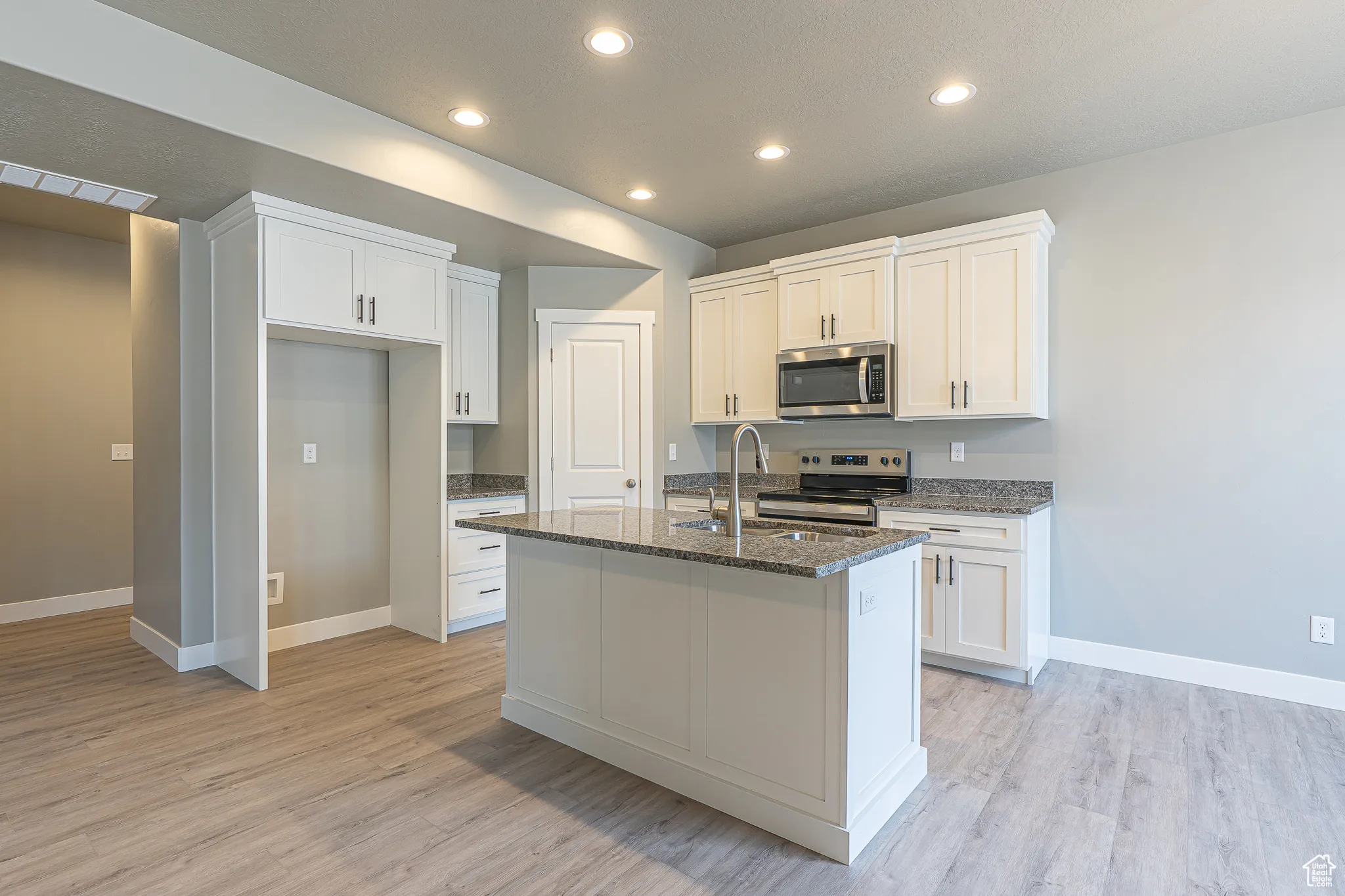 Kitchen with dark stone counters, recessed lighting, appliances with stainless steel finishes, white cabinets, and light wood finished floors