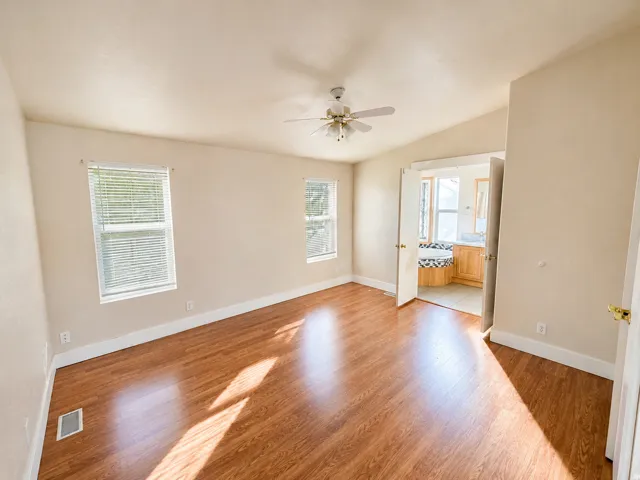 Spacious living area flooded with natural light through multiple windows, featuring rich wood-finish flooring throughout, ceiling fan with integrated lighting, and generous square footage ideal for comfortable entertaining and everyday living