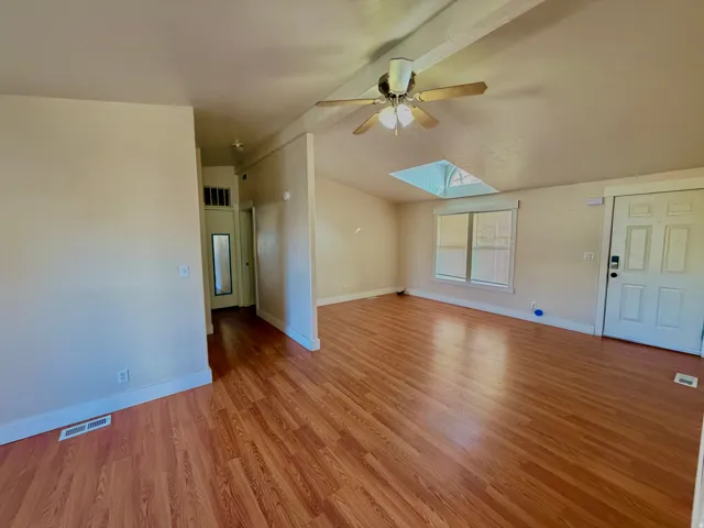 Unfurnished living room with a skylight, vaulted ceiling, light wood finished floors, and ceiling fan