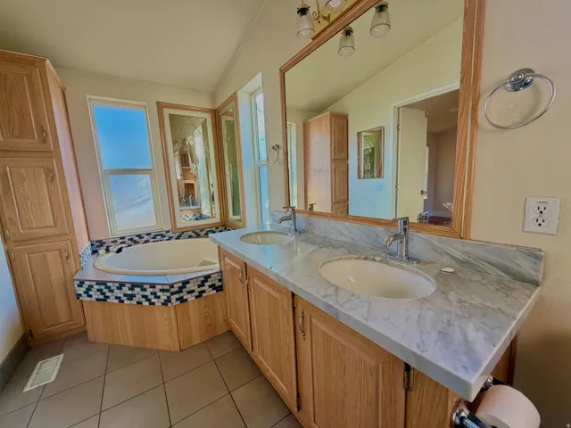 Full bath with double vanity, a bath, and light tile patterned floors