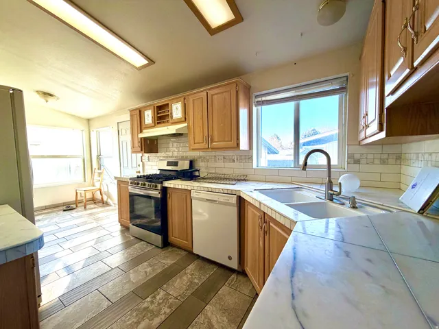 Kitchen with appliances with stainless steel finishes, healthy amount of natural light, under cabinet range hood, vaulted ceiling, and tile countertops