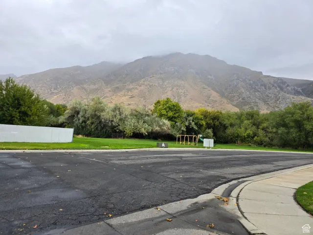 View of asphalt road featuring a mountain view, curbs, view of wooded area, and sidewalks