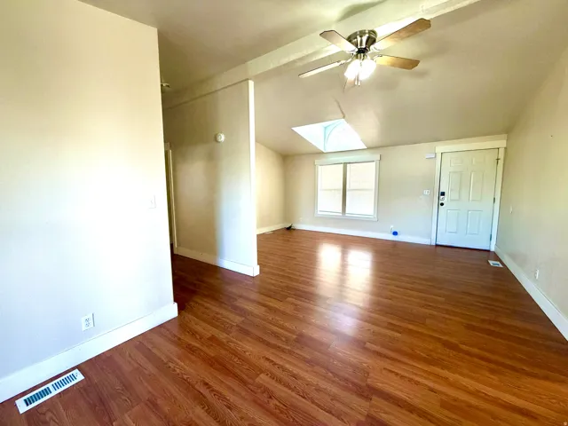 Empty room featuring lofted ceiling, a skylight, dark wood-style flooring, and a ceiling fan