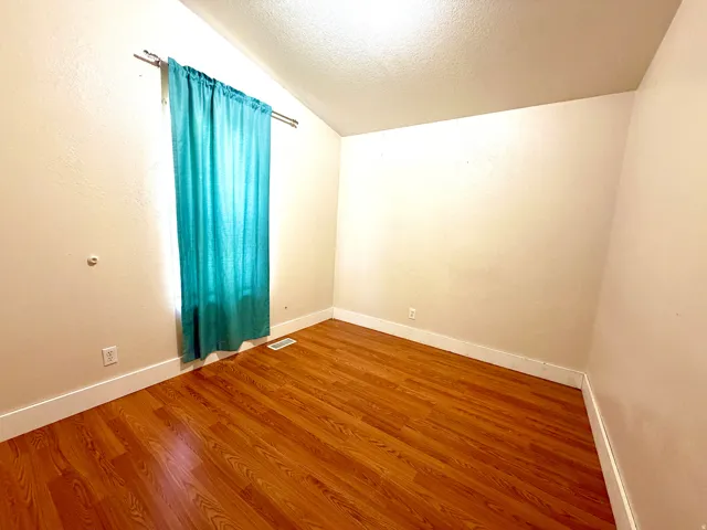 Empty room with a textured ceiling, lofted ceiling, wood finished floors, and a textured wall