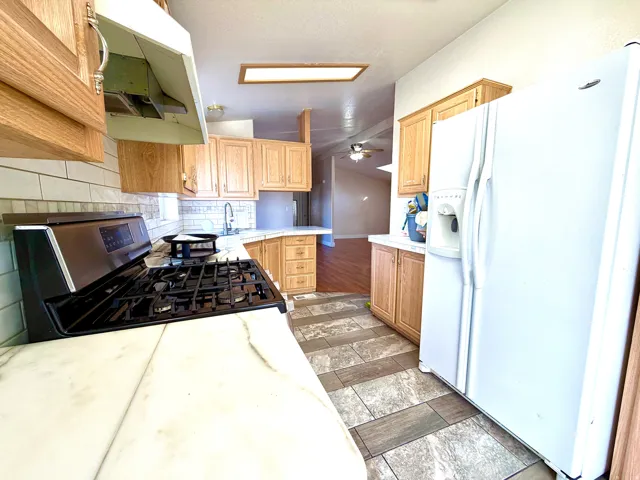 Kitchen with white fridge with ice dispenser, lofted ceiling, decorative backsplash, stainless steel range with gas stovetop, and under cabinet range hood