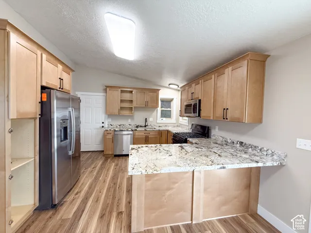 Kitchen featuring open shelves, vaulted ceiling, appliances with stainless steel finishes, a textured ceiling, and light wood-style flooring
