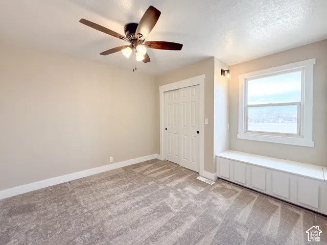 Unfurnished bedroom featuring light colored carpet, a textured ceiling, a ceiling fan, and a closet