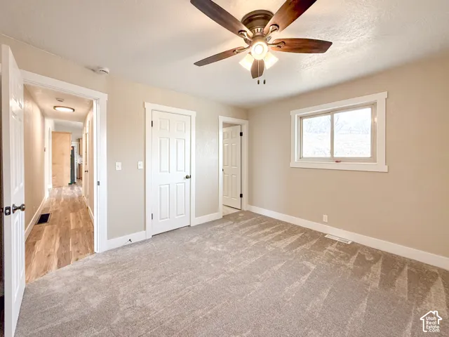 Unfurnished bedroom with light carpet, ceiling fan, and a textured ceiling