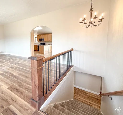 Stairs with arched walkways, wood finished floors, a textured ceiling, and a chandelier