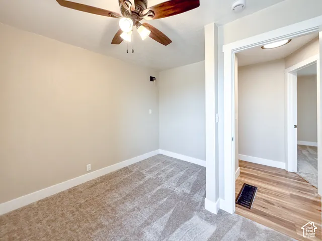 Unfurnished room featuring a ceiling fan, light colored carpet, light wood-style floors, and a smoke detector