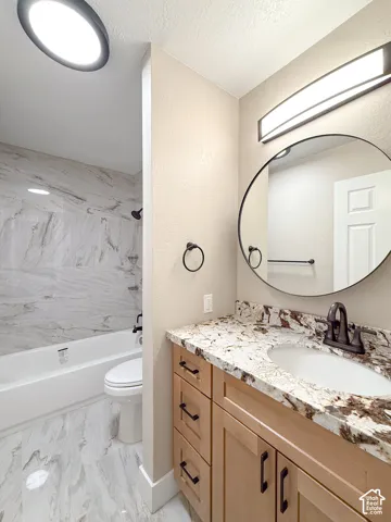 Full bathroom featuring vanity, shower / bath combination, a textured wall, and a textured ceiling