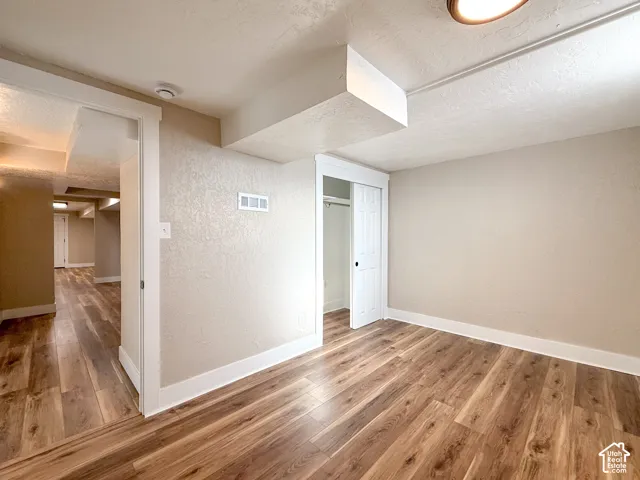 Basement with a textured ceiling, a textured wall, and light wood-style floors