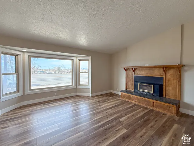 Unfurnished living room with a textured ceiling, a glass covered fireplace, dark wood-style flooring, and lofted ceiling