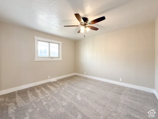 Spare room featuring a textured ceiling, light colored carpet, and a ceiling fan