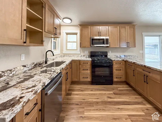 Kitchen featuring appliances with stainless steel finishes, light stone countertops, light wood finished floors, open shelves, and a textured ceiling