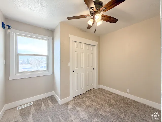 Unfurnished bedroom featuring light carpet, ceiling fan, a textured ceiling, and a closet