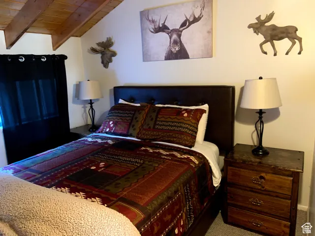 Bedroom with a wood ceiling with exposed beams and carpet flooring
