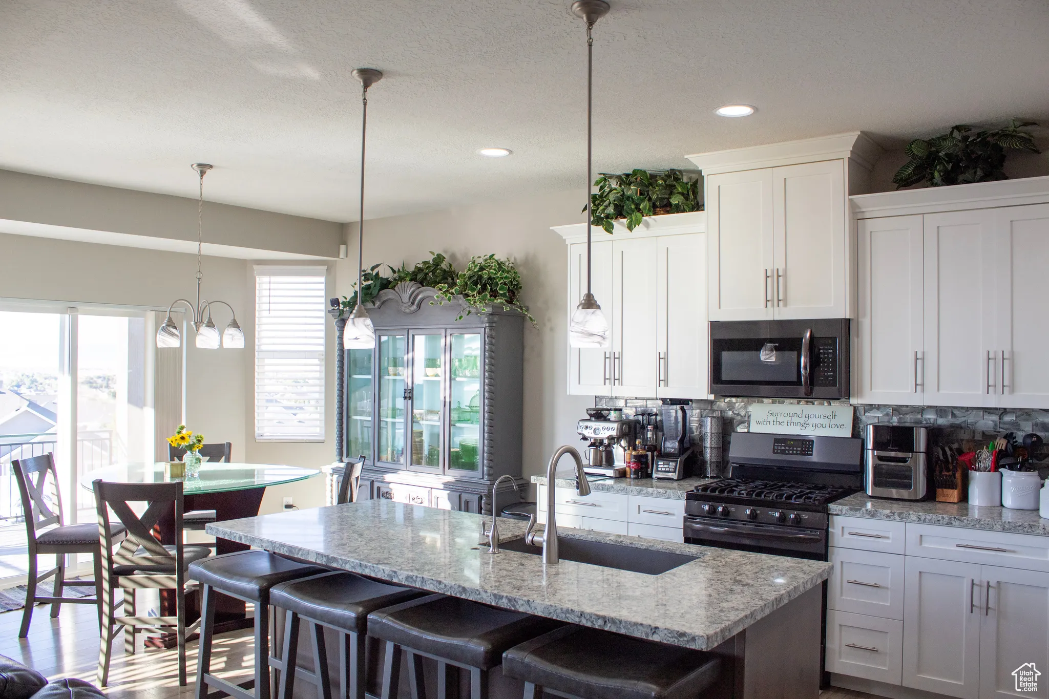 Kitchen with stainless steel appliances, white cabinets, light stone countertops, a kitchen breakfast bar, and recessed lighting