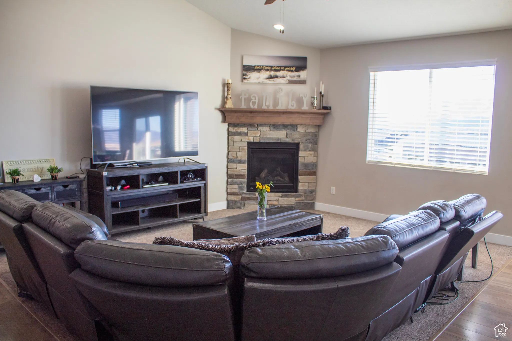 Living room featuring vaulted ceiling, a stone fireplace, wood finished floors, and a ceiling fan