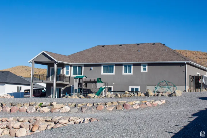 Back of house featuring a patio area, a playground, a mountain view, a shingled roof, and a balcony