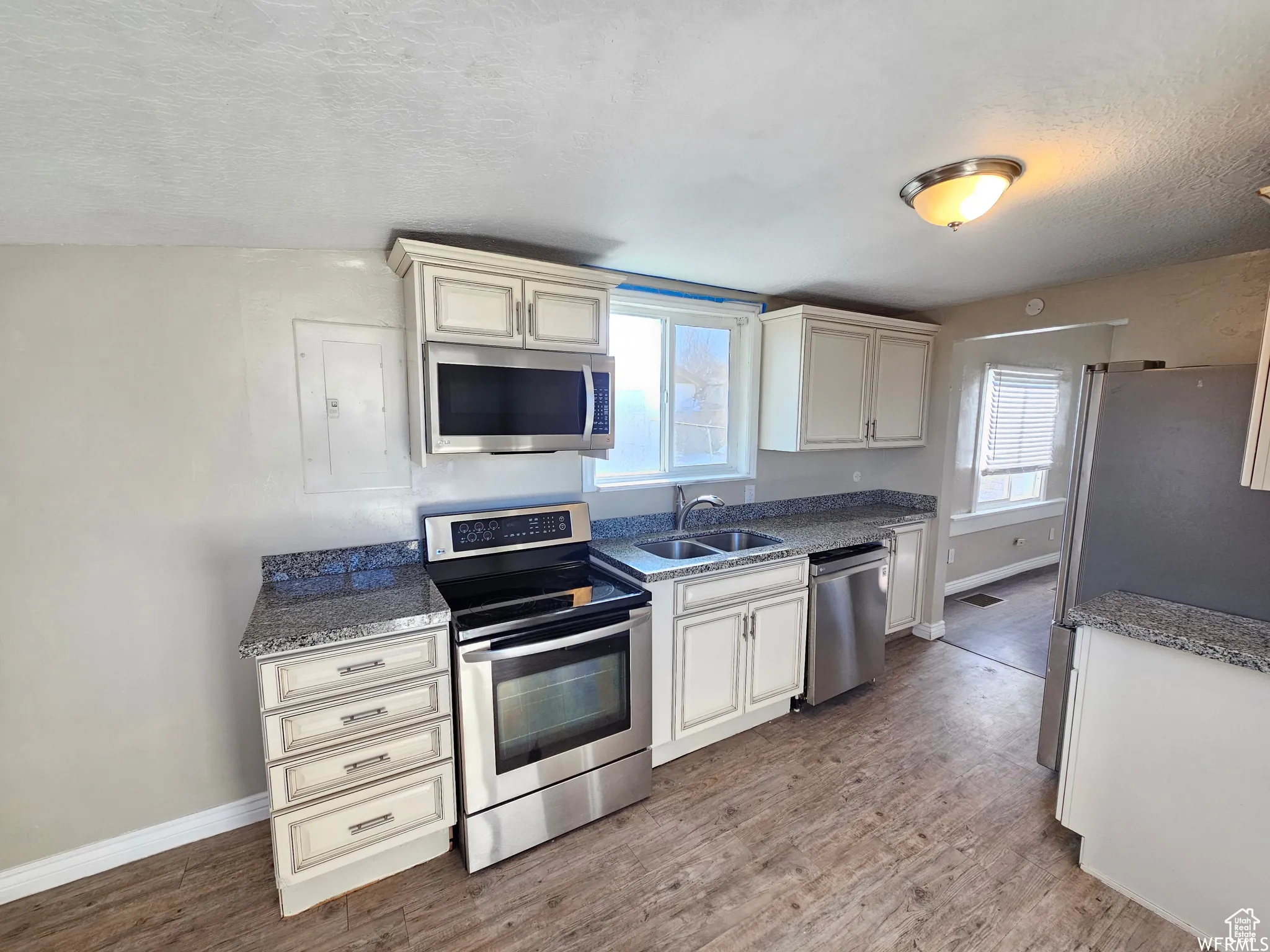 Kitchen featuring appliances with stainless steel finishes, a textured ceiling, light stone countertops, light wood-style flooring, and electric panel