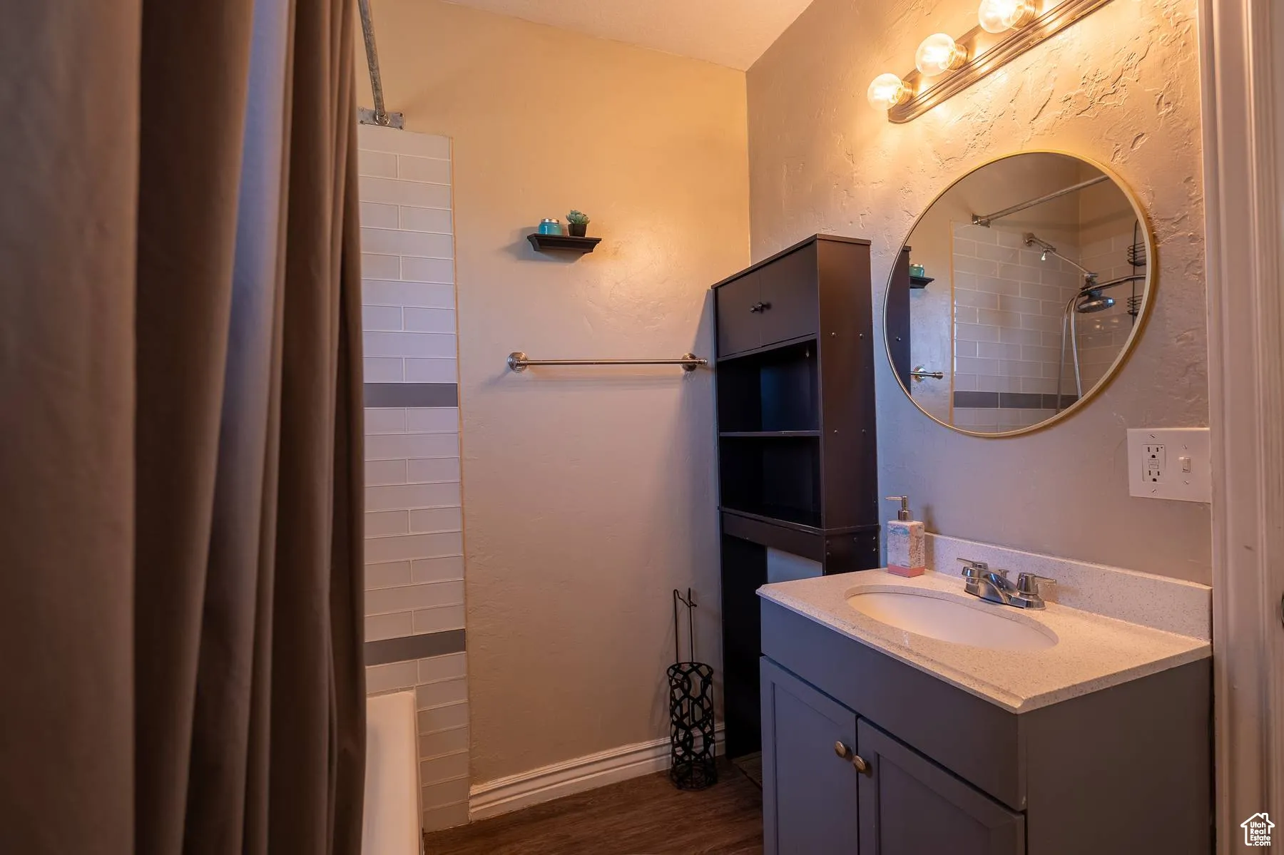 Bathroom with vanity, a textured wall, dark wood-style flooring, and shower / bathtub combination with curtain
