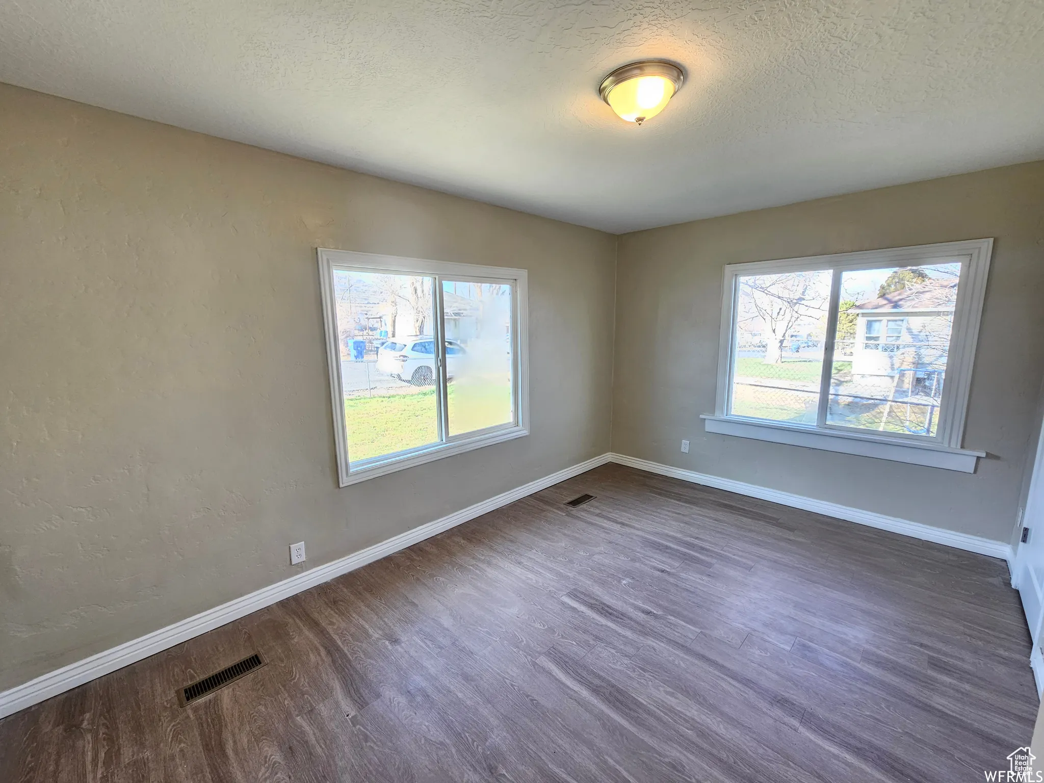 Spare room with dark wood-type flooring, plenty of natural light, a textured ceiling, and a textured wall