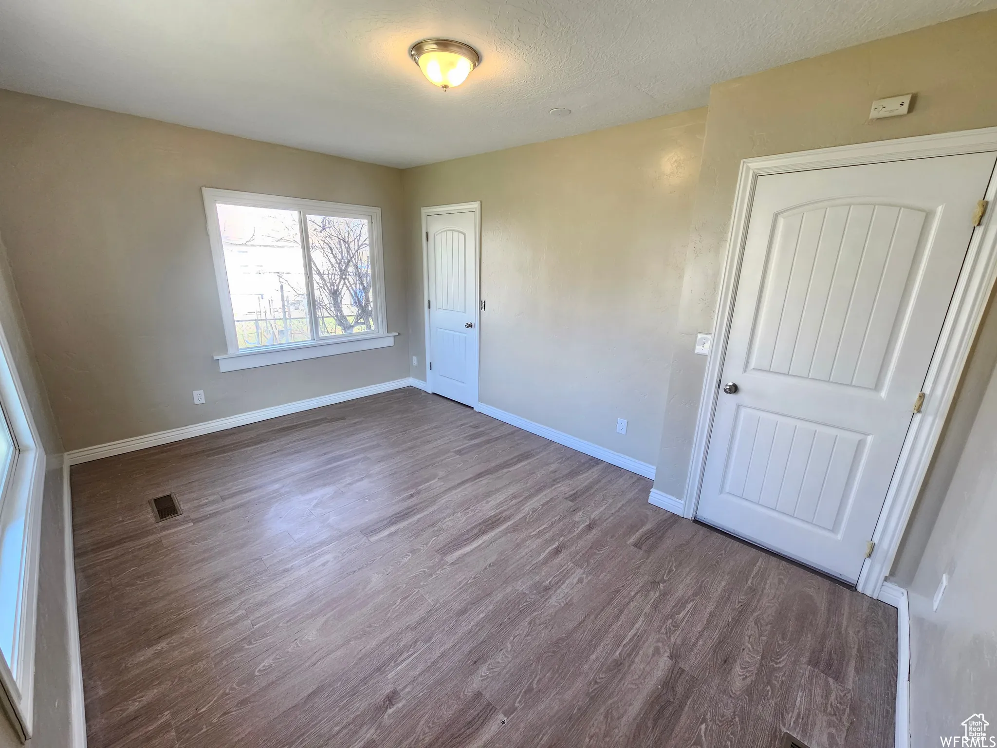 Unfurnished bedroom with dark wood-style flooring and a textured ceiling