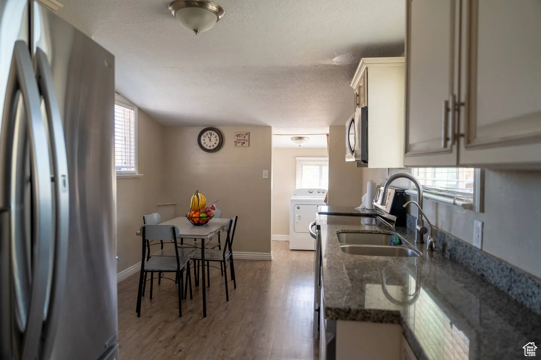 Kitchen featuring stainless steel appliances, dark stone counters, a textured ceiling, light wood finished floors, and washer / clothes dryer