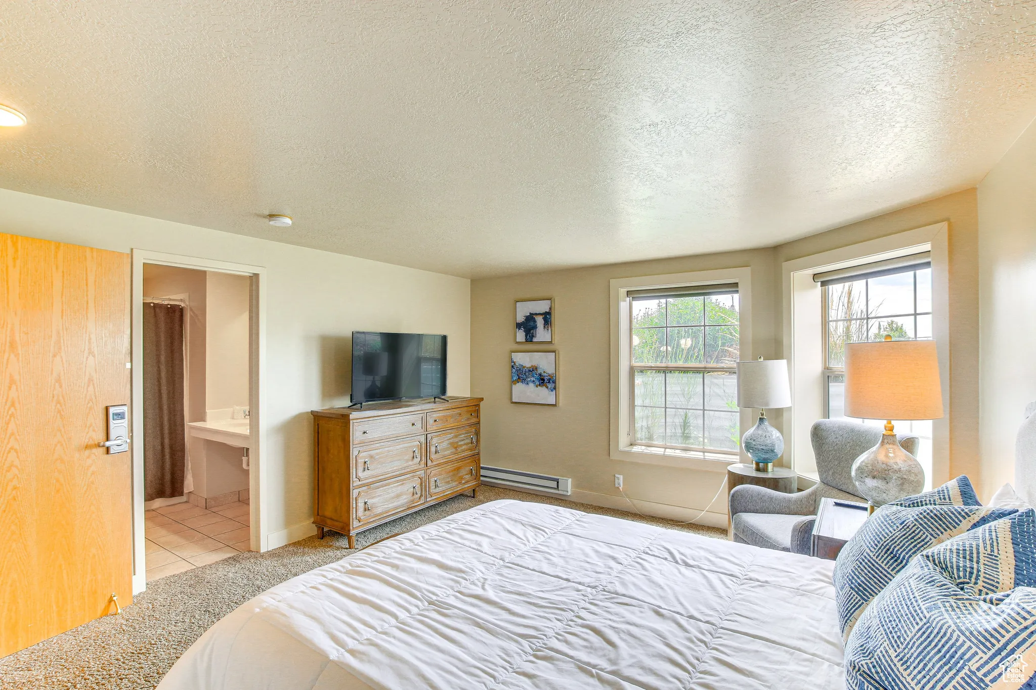 Bedroom featuring a textured ceiling, light tile patterned floors, a baseboard radiator, ensuite bath, and light carpet