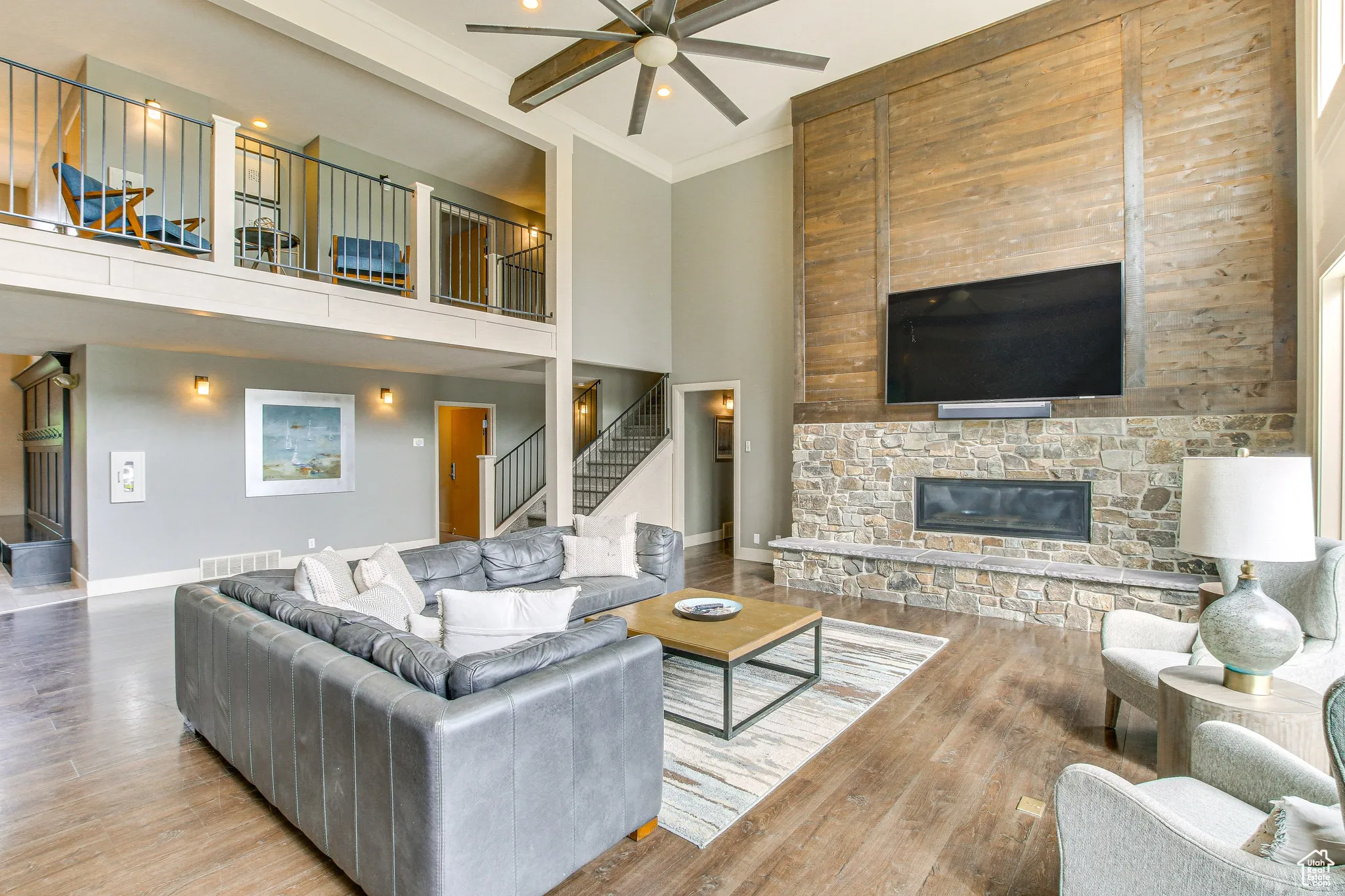 Living area with stairs, ornamental molding, a stone fireplace, wood finished floors, and a high ceiling