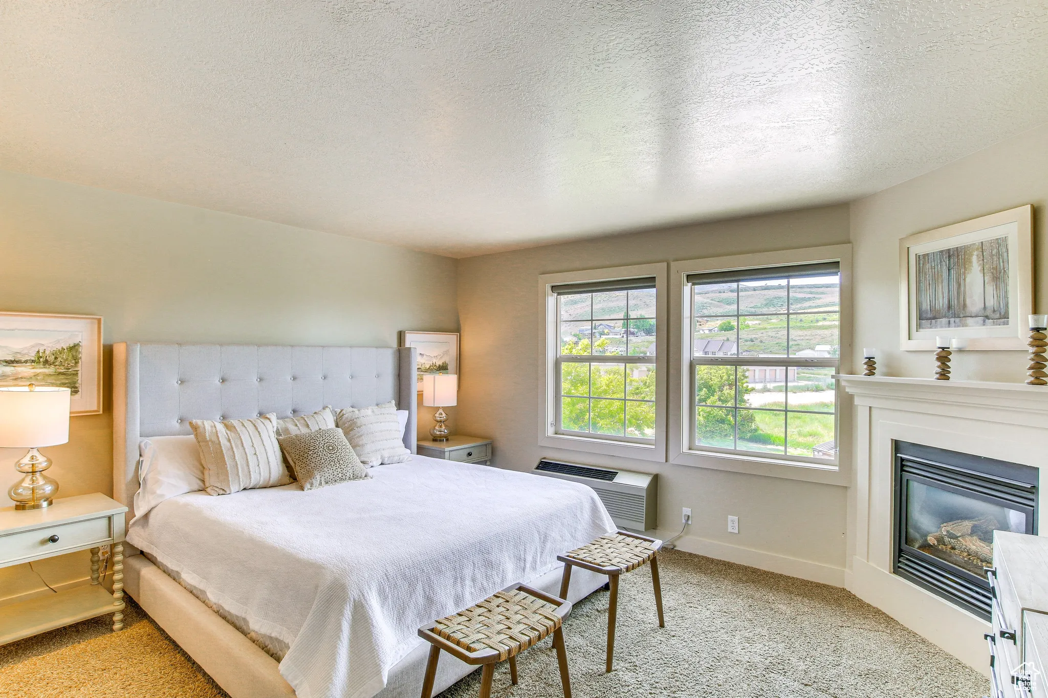 Bedroom with light colored carpet, a textured ceiling, a glass covered fireplace, and an AC wall unit